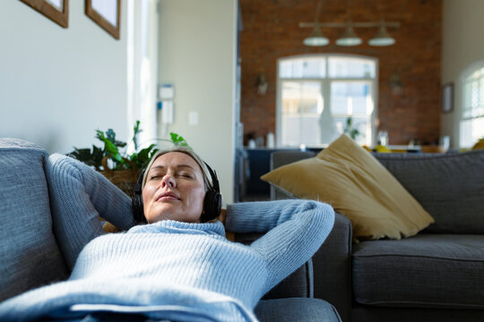 Relaxed senior caucasian woman in living room lying on sofa, wearing headphones