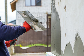 Construction worker covering house wall with adhesive cement glue berore installing styrofoam insulation sheets for thermal protection. - obrazy, fototapety, plakaty