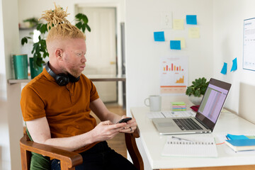 Albino african american man with dreadlocks working from home and using smartphone laptop