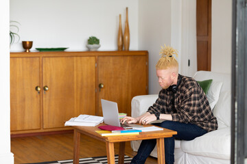 Albino african american man with dreadlocks working from home and using laptop