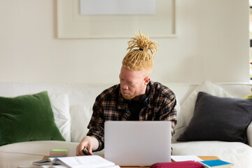 Albino african american man with dreadlocks working from home and using laptop