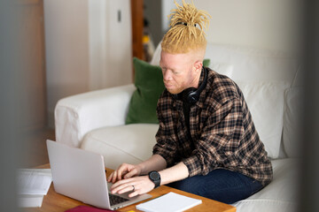 Albino african american man with dreadlocks working from home and using laptop