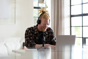 Happy albino african american man with dreadlocks working from home and making podcast