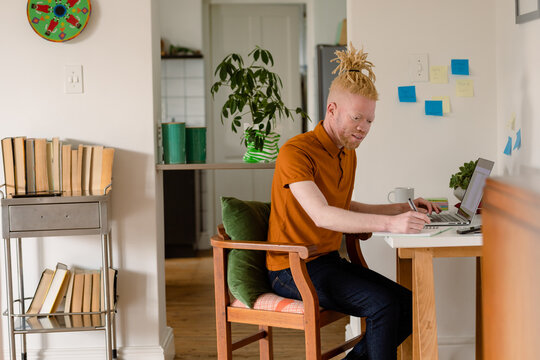 Albino african american man with dreadlocks working from home and using laptop
