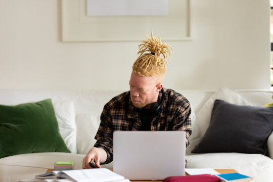 Albino african american man with dreadlocks working from home and using laptop