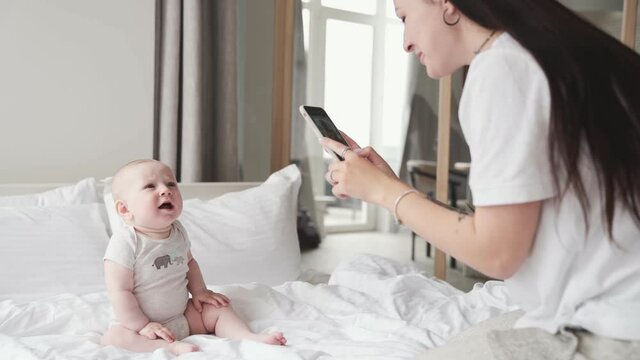 Mom taking a photo of her baby sitting on the bed