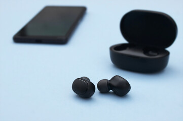 Smartphone and wireless headphones or earbuds with charging case on bright blue background.