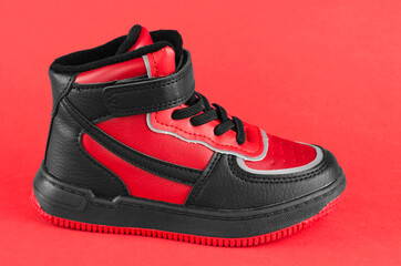 Children's red-black sneakers on a red background. Children's leather shoes close up