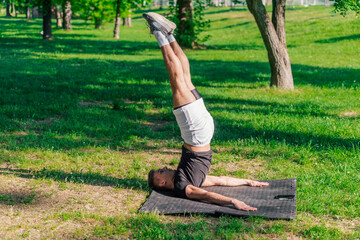 Young sporty handsome man practicing yoga in the park and doing the plow pose..