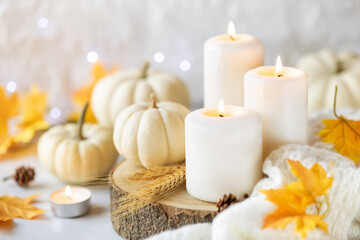 Obraz na płótnie Canvas Hello Autumn or Happy Thanksgiving concept. White burning candles with white pumpkins at the background, knitted plaid and autumnal leaves. Shallow depth of field