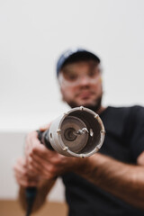 Construction worker electrician or plumber wearing a protective mask with a hammer drill and drill bit bit on concrete - bottom view focus on the drill