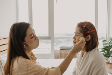 Asian woman makeup artist is at work and wearing makeup on her model.