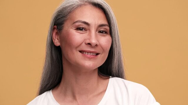 A smiling asian mature woman looking at the camera in the beige studio