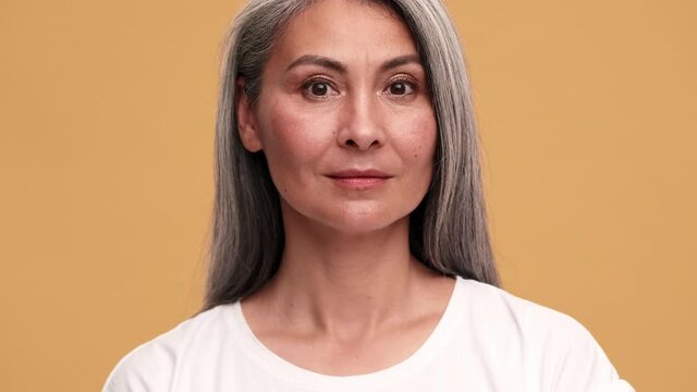 A confident asian mature woman opening her eyes at the camera in the beige studio