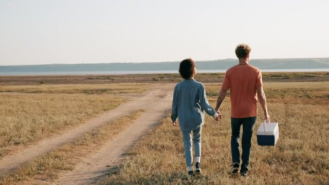 Rear view of a multinational couple going to the estuary for a picnic