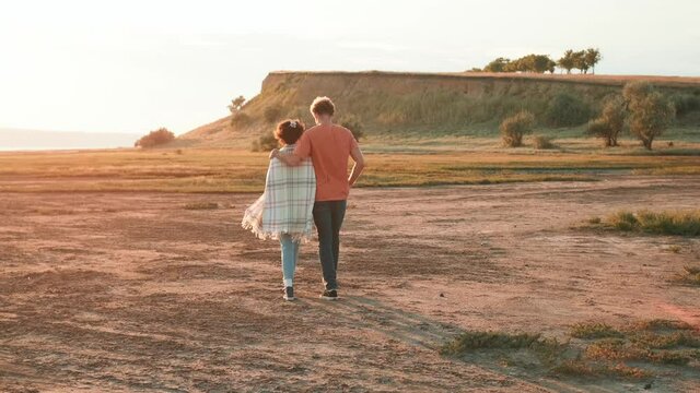 Rear view of a beautiful multinational couple hugging and going to the estuary 