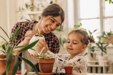 Mixed race family young happy woman and her daughter is planting and watering houseplants at...