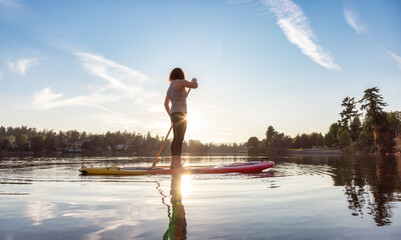 Adventurous Caucasian Adult Woman Paddling on a Stand up Paddle Board in water at a city park....