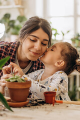 Happy mixed race family young woman with her daughter is planting houseplants at home.Home...