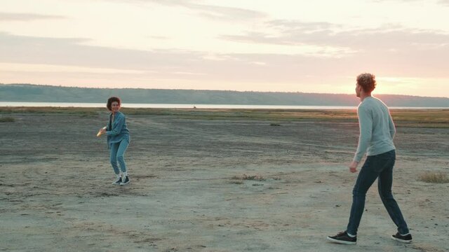 Smiling multinational couple throwing frisbee to each other while standing among the estuary 