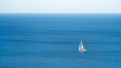 alone white sailboat rides in summer day at blue sea with horizon and copy space in frame ratio 16 to 9