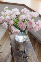 Beautiful autumn flowers in modern vase and scissors on rustic wooden background. Pink asters flowers in sunny light. Hello autumn, floral arrangement for fall holidays in countryside home