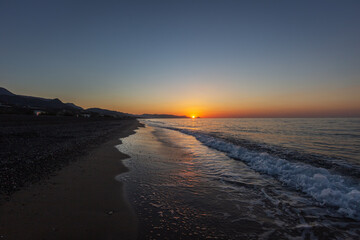 Sandy beach at sunrise with beautiful sea waves in the background of mountain and beautiful colorful sky with sun