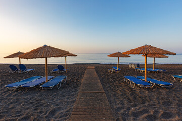 sandy beach and a wooden path in the middle leads between blue umbrellas to the beautiful blue calm sea