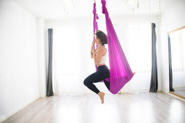 young woman practicing aerial yoga fly yoga alone in studio with hammock moving preparing for seahorse pose yoga fitness exercise training, fit dancer gymnastics dance health pilates