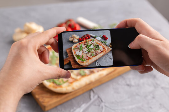 Male photographing on smartphone pizza with ham and mushrooms. Social networks and delivery food application concept.