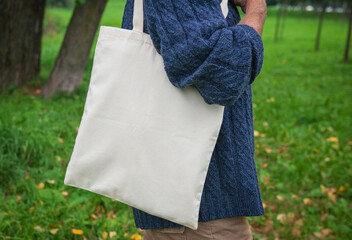 Stylish man holding white blank canvas tote shopping bag