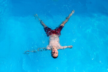From above of carefree relaxed young handicapped male with amputated arm lying on blue water...