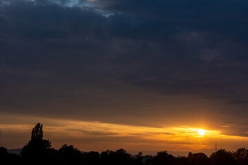 Dramatic orange sunset in a cloudy sky with trees