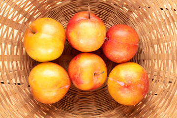Several juicy sweet yellow-red plums in a straw bowl, close-up, top view.