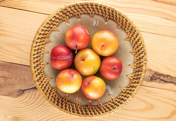 Several juicy sweet yellow-red plums on a ceramic dish on a wooden table, close-up, top view.