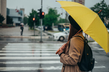 Woman standing on a crossroad and holding a yellow umbrella
