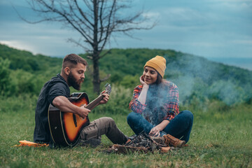 Naklejka na ściany i meble Couple of campers sitting by the camp fire and playing guitar