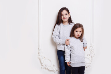 Two adorabile sisters posing together on white background, smiling and looking at camera.