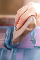closeup on a female hand with painted nails that floods a screen printing frame with paint by help...