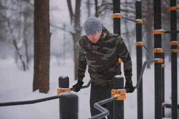 Training outside in winter in a snowfall. a man does push-ups on the uneven bars in a snowstorm	