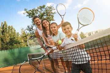 Happy family with tennis rackets on court outdoors - obrazy, fototapety, plakaty