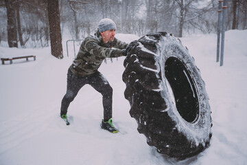A man is engaged in functional training with a large tire. The training takes place outside in...