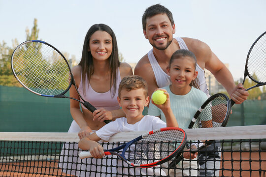 Happy family with tennis rackets on court outdoors - Powered by Adobe