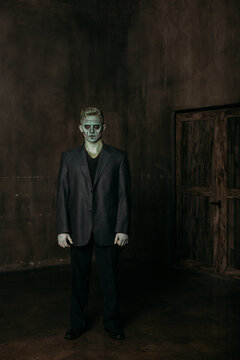 A man in the image of Frankenstein, green makeup, dark jacket, Halloween. The image of a man on Halloween. full-length photo in a dark room