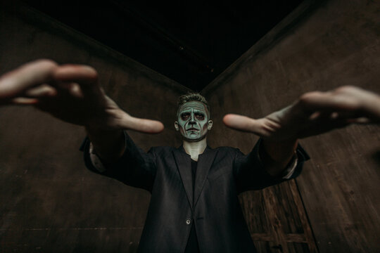 A man in the image of Frankenstein, green halloween makeup, dark jacket, Halloween, arms outstretched like a zombie. The image of a man on Halloween.