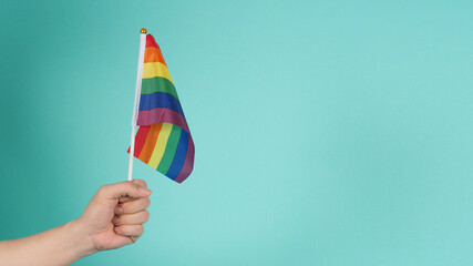 LGBT concept.Hand is holding a rainbow flag on mint green or tiffany blue background.