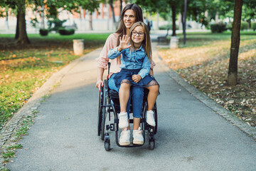 A mother in a wheelchair enjoys with her daughter outside on a beautiful sunny day.