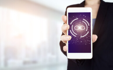 Infinite concept. Hand hold white smartphone with digital hologram infinity sign on light blurred background.