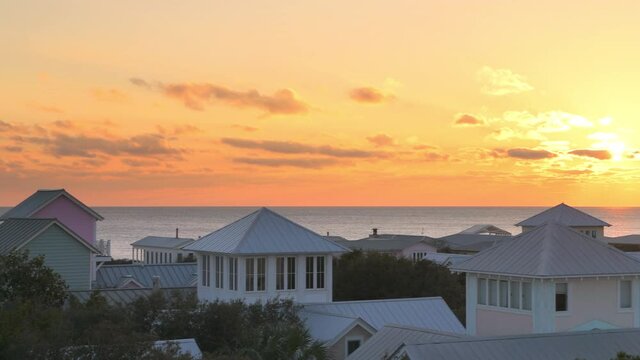 Aerial horizontal panning view on colorful yellow sunset with sea ocean landscape of Gulf of Mexico in Seaside, Florida from wooden rooftop terrace buildings houses cityscape