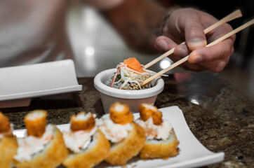 man's hand dips a piece of sushi in sauce